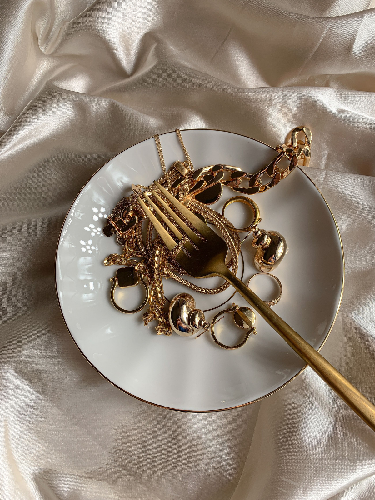 Gelaagde gouden kettingen op crème stof met zachtroze bloemen